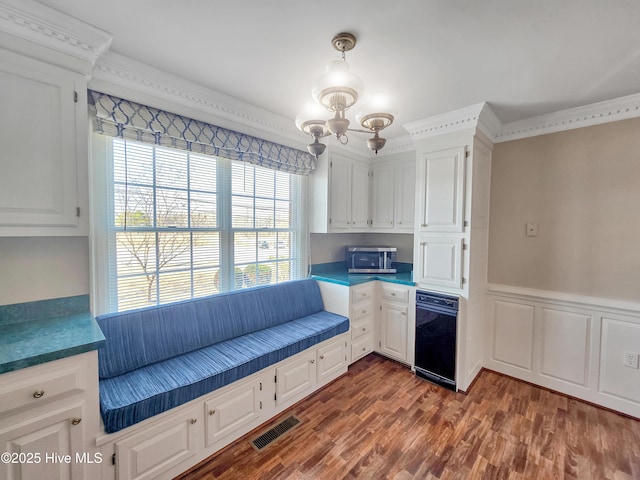 kitchen featuring a wainscoted wall, visible vents, ornamental molding, dark wood-type flooring, and white cabinetry
