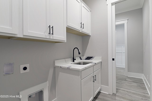 clothes washing area with baseboards, cabinet space, electric dryer hookup, a sink, and light wood-type flooring