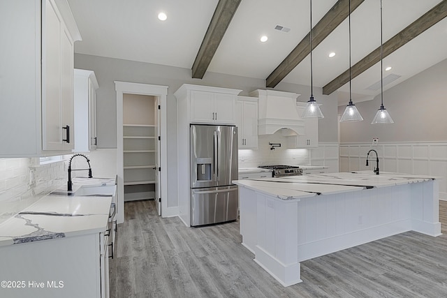 kitchen with premium range hood, a sink, stainless steel appliances, white cabinetry, and beamed ceiling