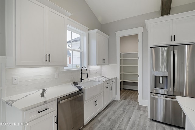 kitchen featuring backsplash, vaulted ceiling, light wood-style floors, stainless steel appliances, and a sink