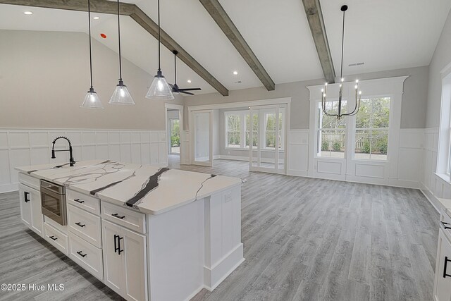 kitchen with a center island with sink, light wood-style flooring, white cabinetry, a chandelier, and vaulted ceiling with beams