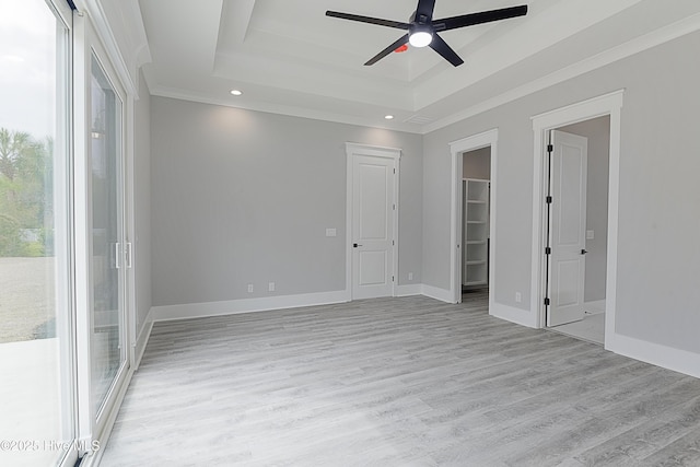 spare room featuring ornamental molding, a tray ceiling, light wood finished floors, baseboards, and ceiling fan