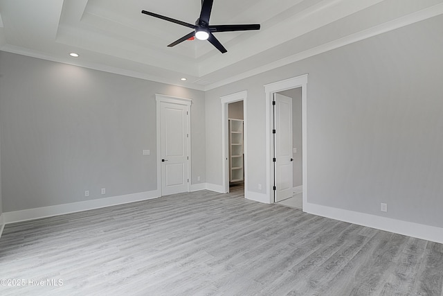 empty room featuring a tray ceiling, wood finished floors, baseboards, and ceiling fan