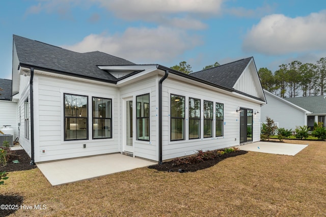 rear view of property with a lawn, a shingled roof, and a patio