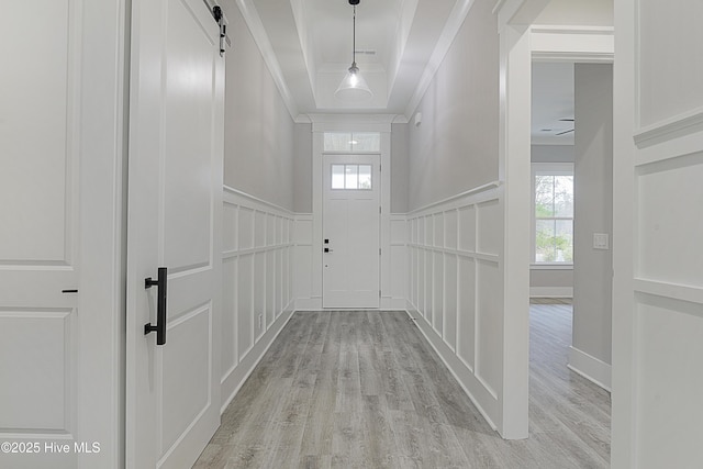 hallway featuring a barn door, a decorative wall, crown molding, and light wood finished floors