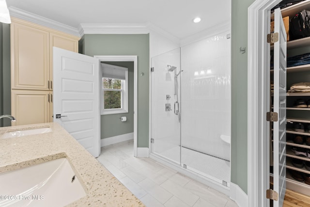 bathroom featuring a sink, a stall shower, a walk in closet, baseboards, and ornamental molding