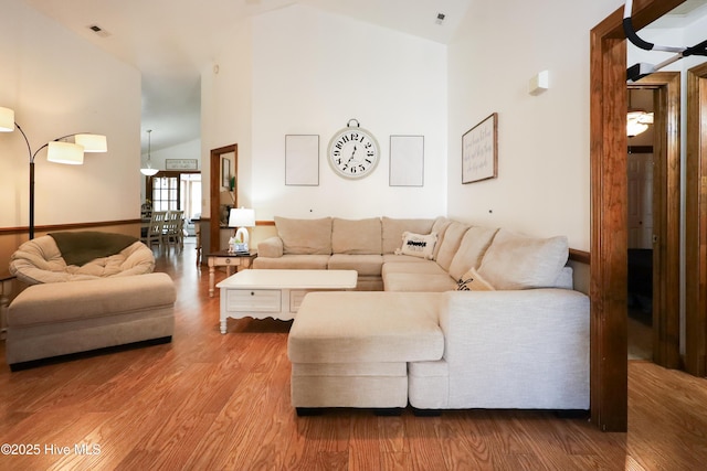 living area with wood finished floors, visible vents, and high vaulted ceiling