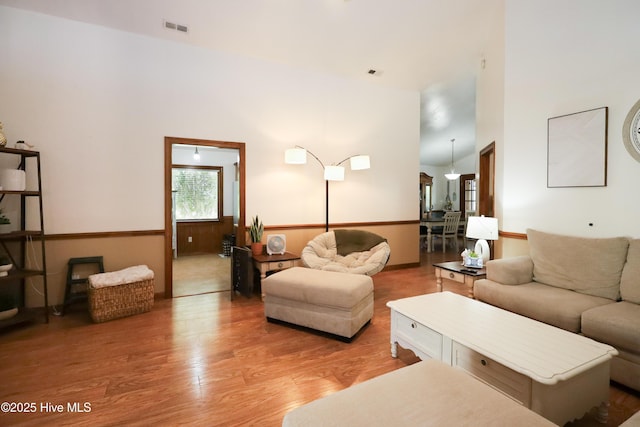 living room featuring a towering ceiling, visible vents, and light wood-type flooring