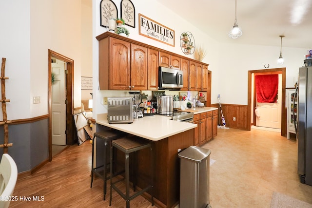 kitchen with wainscoting, a breakfast bar area, light countertops, a peninsula, and appliances with stainless steel finishes