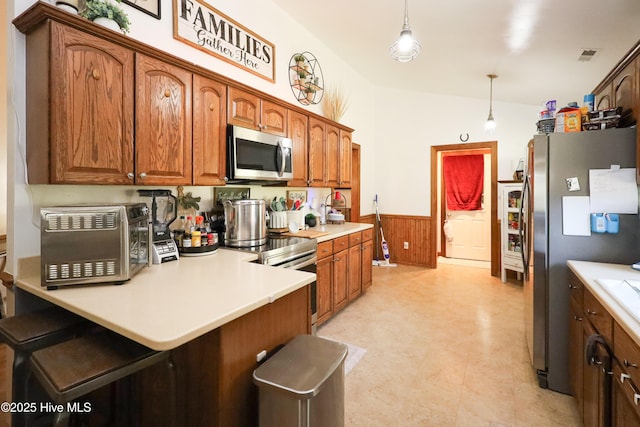kitchen featuring hanging light fixtures, a wainscoted wall, light countertops, a peninsula, and appliances with stainless steel finishes