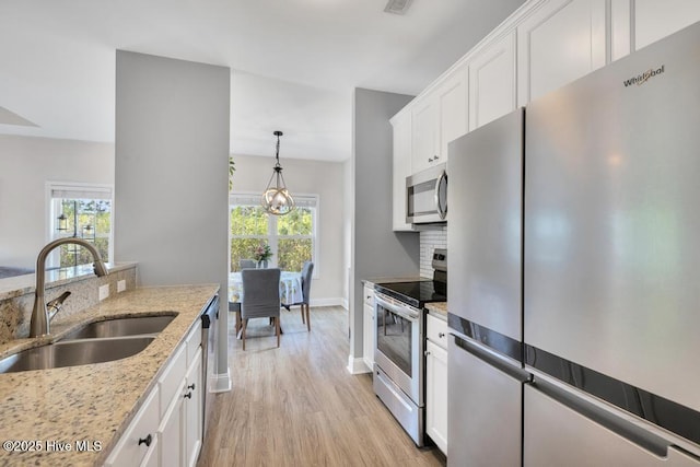 kitchen with white cabinets, a sink, stainless steel appliances, a wealth of natural light, and light wood-type flooring