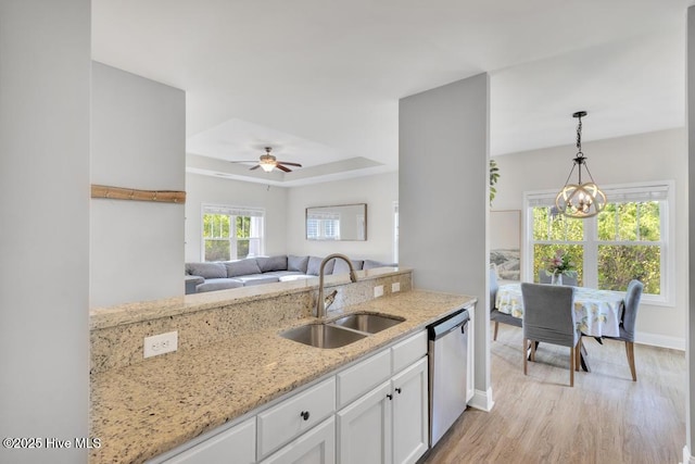 kitchen featuring stainless steel dishwasher, a sink, light stone counters, light wood-style floors, and white cabinetry