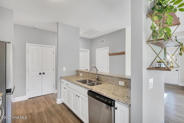 kitchen with light stone countertops, white cabinetry, a sink, light wood-style flooring, and stainless steel appliances