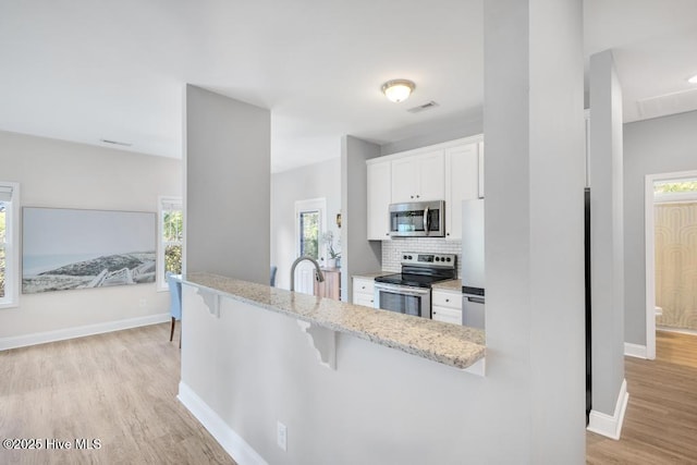 kitchen featuring a breakfast bar area, light wood-type flooring, white cabinetry, light stone counters, and stainless steel appliances