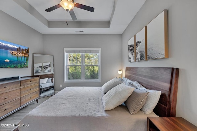 bedroom featuring a raised ceiling, ceiling fan, wood finished floors, and visible vents