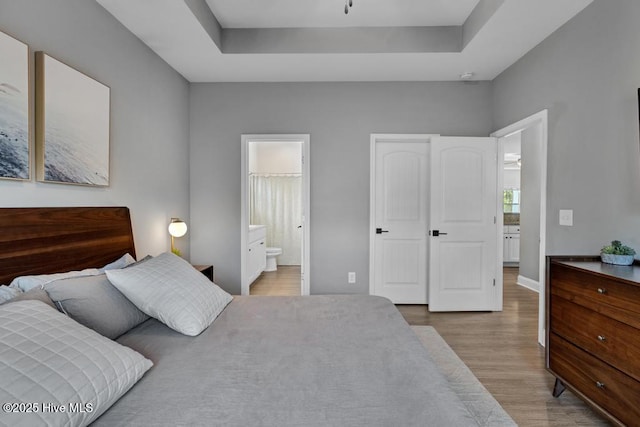bedroom featuring a tray ceiling, wood finished floors, and connected bathroom