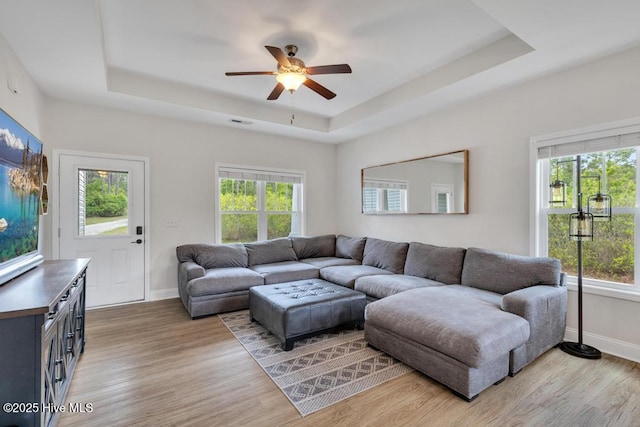 living room with light wood-style flooring, ceiling fan, a tray ceiling, and a healthy amount of sunlight