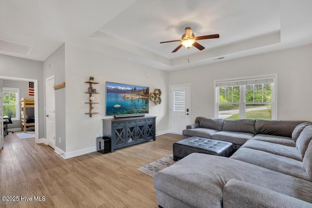 living area with baseboards, ceiling fan, a tray ceiling, and light wood-style flooring