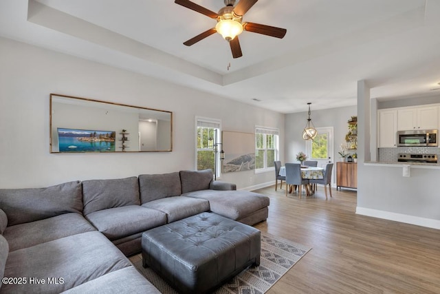 living area featuring light wood-style floors, a ceiling fan, baseboards, and a tray ceiling