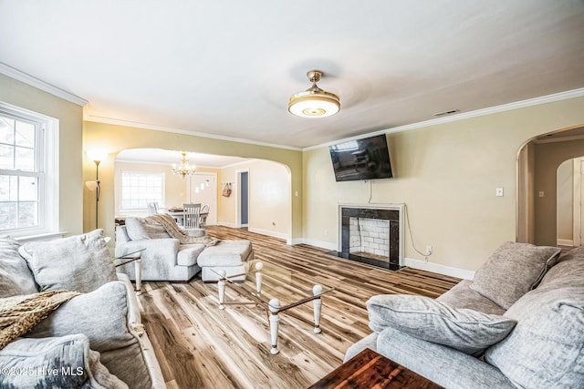 living room featuring wood finished floors, baseboards, an inviting chandelier, a fireplace with flush hearth, and arched walkways