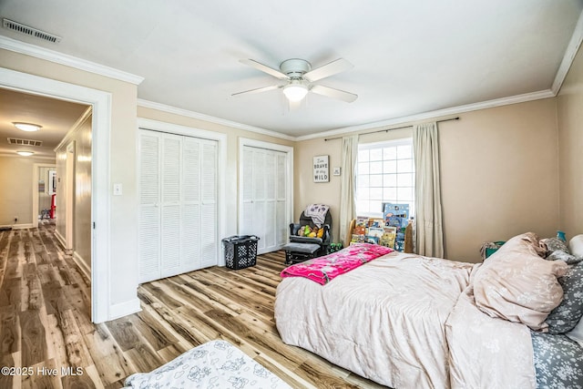bedroom featuring visible vents, ornamental molding, multiple closets, and wood finished floors