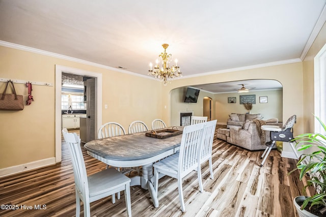 dining space featuring arched walkways, light wood-type flooring, an inviting chandelier, and ornamental molding