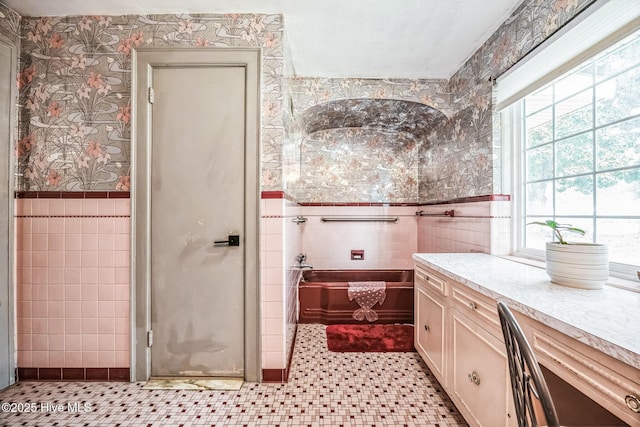 bathroom featuring tile walls, a bath, wainscoting, and wallpapered walls
