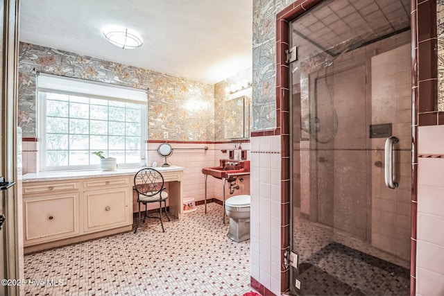 full bath featuring wallpapered walls, toilet, wainscoting, a stall shower, and tile walls