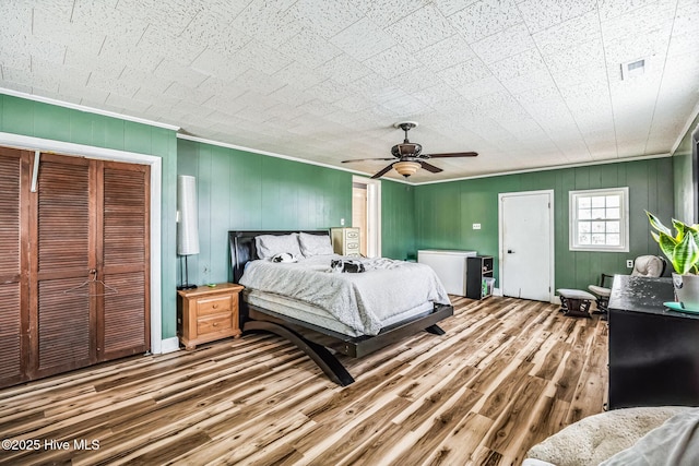 bedroom with a ceiling fan, wood finished floors, visible vents, a closet, and crown molding