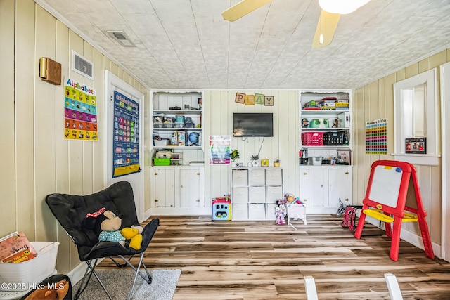 recreation room featuring visible vents, built in shelves, a ceiling fan, and wood finished floors