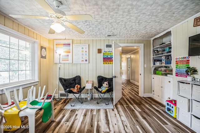 sitting room featuring ceiling fan, baseboards, wood finished floors, and crown molding