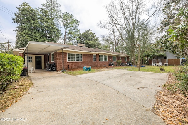 ranch-style house featuring an attached carport, fence, driveway, a chimney, and brick siding