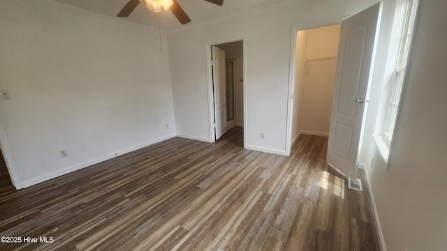 unfurnished bedroom featuring a closet, a walk in closet, baseboards, dark wood-type flooring, and visible vents