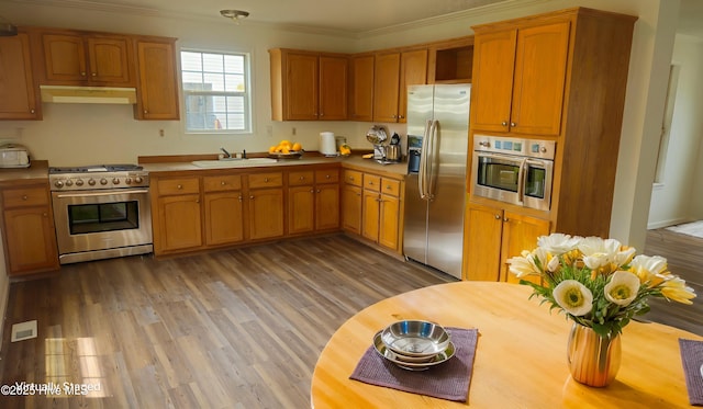 kitchen featuring under cabinet range hood, stainless steel appliances, a sink, light wood-type flooring, and crown molding