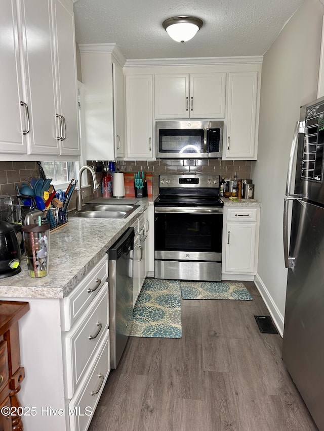 kitchen with dark wood-style flooring, white cabinets, a sink, and appliances with stainless steel finishes