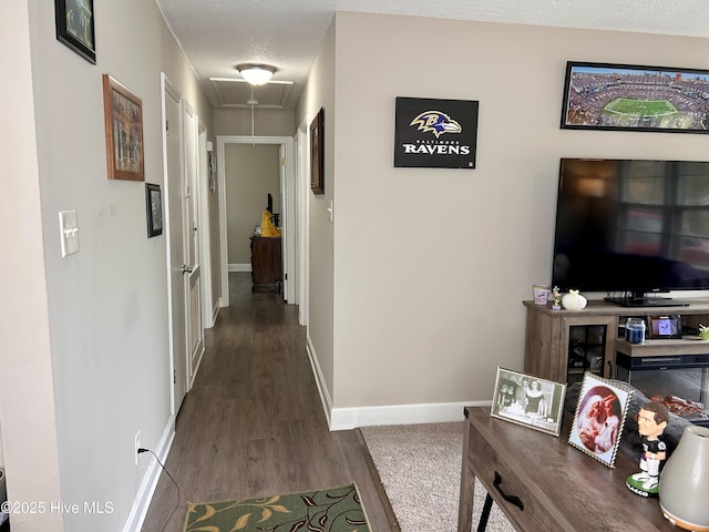 hallway featuring attic access, baseboards, wood finished floors, and a textured ceiling