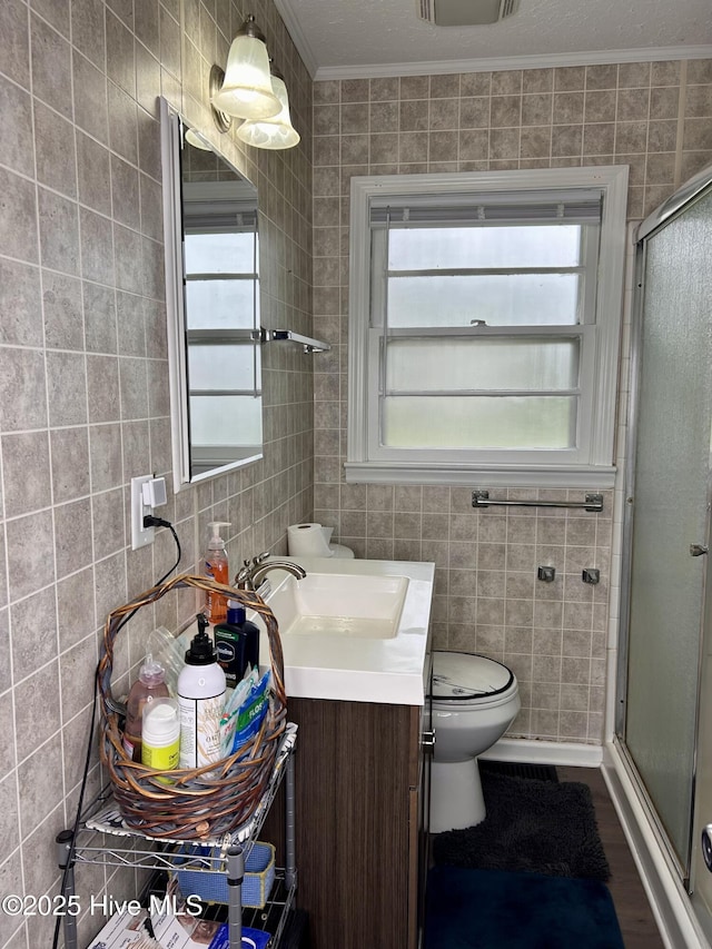 full bathroom featuring a stall shower, crown molding, toilet, vanity, and tile walls