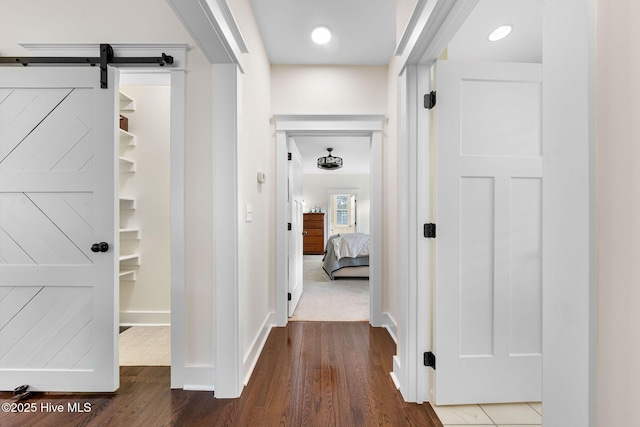 corridor featuring baseboards, wood finished floors, and a barn door