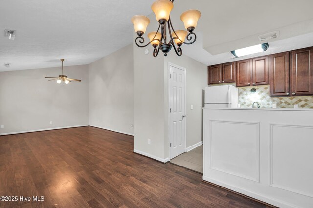 kitchen featuring backsplash, lofted ceiling, ceiling fan with notable chandelier, freestanding refrigerator, and dark wood-style floors
