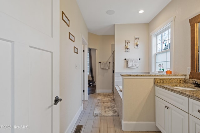full bathroom with wood finished floors, visible vents, vanity, baseboards, and a tub