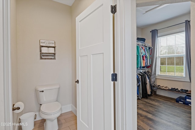 bathroom with baseboards, wood finished floors, a walk in closet, and toilet