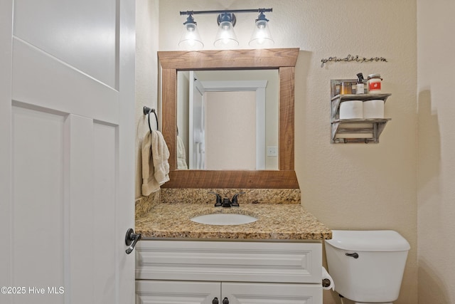 half bath with a textured wall, vanity, and toilet