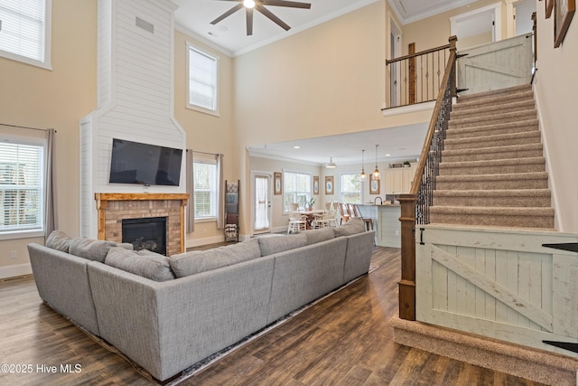 living area featuring ceiling fan, crown molding, a brick fireplace, and stairs