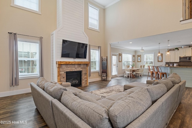 living room featuring dark wood-style floors, baseboards, a towering ceiling, crown molding, and a fireplace