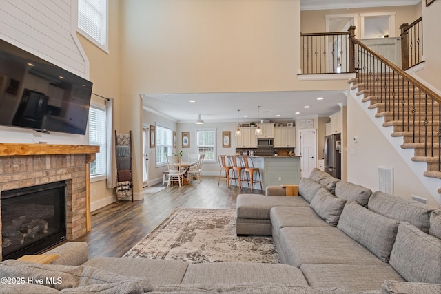 living room with visible vents, a towering ceiling, a brick fireplace, and ornamental molding
