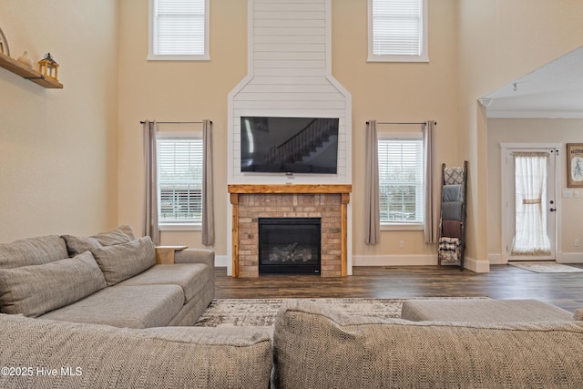 living area featuring baseboards, ornamental molding, a brick fireplace, and wood finished floors
