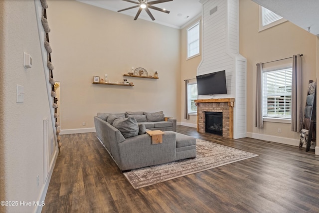 living room featuring ceiling fan, baseboards, a brick fireplace, and wood finished floors