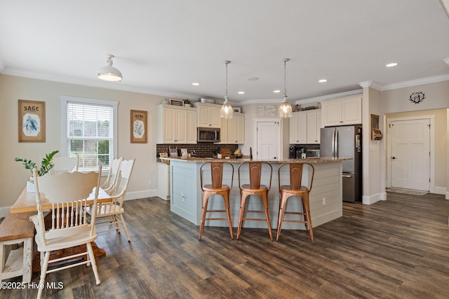 kitchen with an island with sink, appliances with stainless steel finishes, dark wood finished floors, backsplash, and ornamental molding