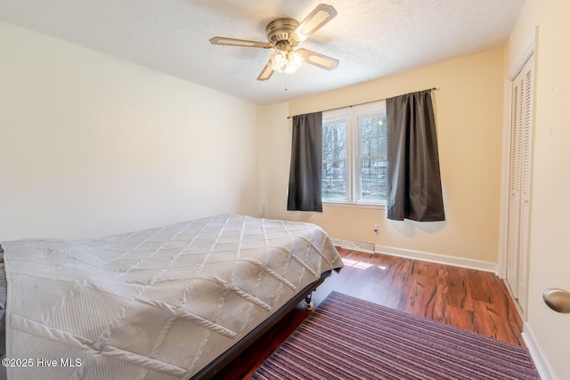 bedroom featuring visible vents, baseboards, wood finished floors, a closet, and ceiling fan