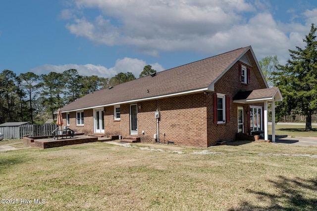 rear view of house featuring roof with shingles, brick siding, entry steps, an outdoor structure, and a yard
